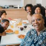 Multi-generational African American family enjoying a meal together, with a smiling older woman making a peace sign
