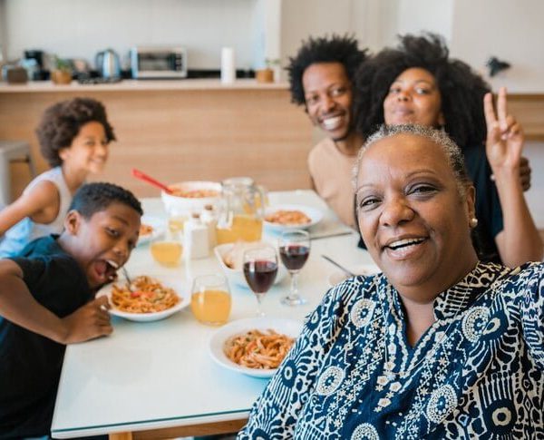 Multi-generational African American family enjoying a meal together, with a smiling older woman making a peace sign