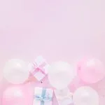 White gift boxes with pink and blue ribbons surrounded by pink and white balloons on a soft pink background