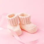 Pair of pale pink hand-knitted baby booties on a pink background with ribbon