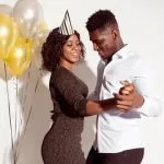 African American couple dancing together at a party with gold and white balloons in the background