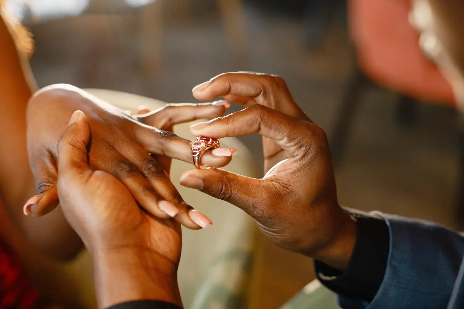 Close-up of a couple's hands as one person places an elegant engagement ring on the other's finger, symbolizing their commitment.