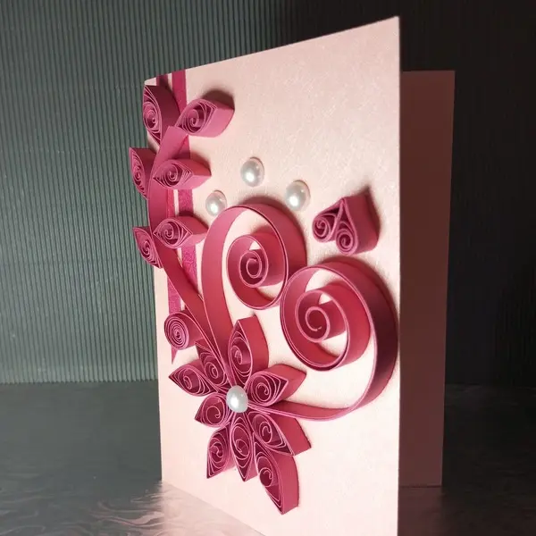 Handmade greeting card featuring pink quilled paper art in the shape of a heart with floral elements and pearl embellishments