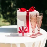 Wedding Gifts Kenya. Two white gift boxes with red ribbons and two pink champagne flutes on a white tablecloth.