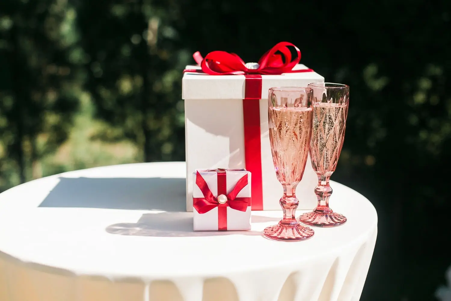 Wedding Gifts Kenya. Two white gift boxes with red ribbons and two pink champagne flutes on a white tablecloth.